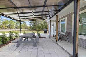 A covered patio with a picnic table and chairs, a grill, and a view of the backyard.