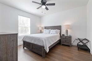 A bedroom with a wooden bed, bedside lamps, a ceiling fan, and a window with blinds.