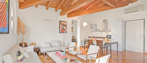 Un vaste espace de vie doté d’un plafond en bois, de meubles blancs et d’une cuisine située au fond de la pièce.