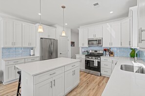 A modern kitchen with white cabinets, stainless steel appliances, a large island, and a tiled backsplash.