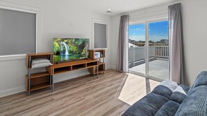 Ett modernt vardagsrum med en platt-TV på ett träställ, en soffa och en balkong med utsikt över staden.