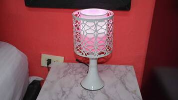 Eine weiße Tischlampe mit rosa Schirm auf einem Marmortisch vor einer roten Wand.