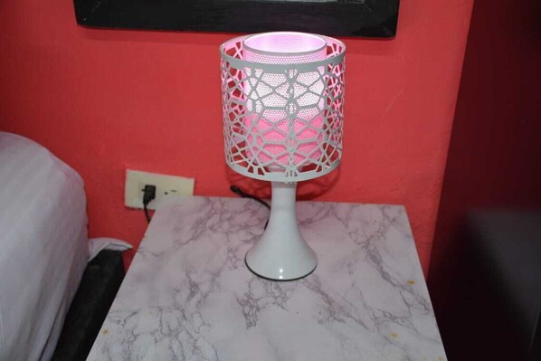 Una lámpara de mesa blanca con pantalla rosa sobre una mesa de mármol, frente a una pared roja.