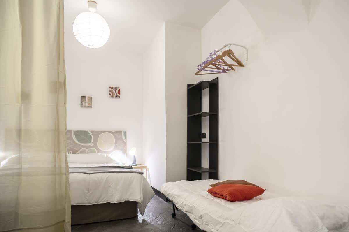 Une chambre à coucher comprenant un lit, une table de chevet, un luminaire suspendu et une étagère fixée au mur.
