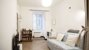 Habitació petita i ben il·luminada amb un llit, una estant de llibres, un radiador i una finestra.