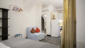 Una habitació d'hotel amb un llit, un otomà estampat, un petit tamboret i un armari.