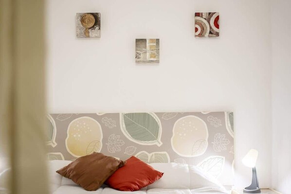 A bedroom with a patterned headboard, a bed with two pillows, and a bedside table with a lamp.