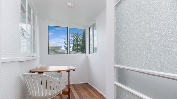 A small room with a wooden table and a white chair, a window with a view of trees and a building, and a textured wall. - The Castaway (Emu Park)