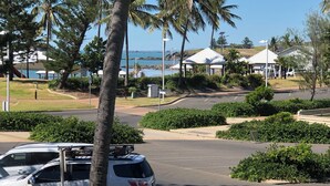 A parking area with a white SUV, palm trees, and a view of a beach and ocean in the background. - The Castaway (Emu Park)
