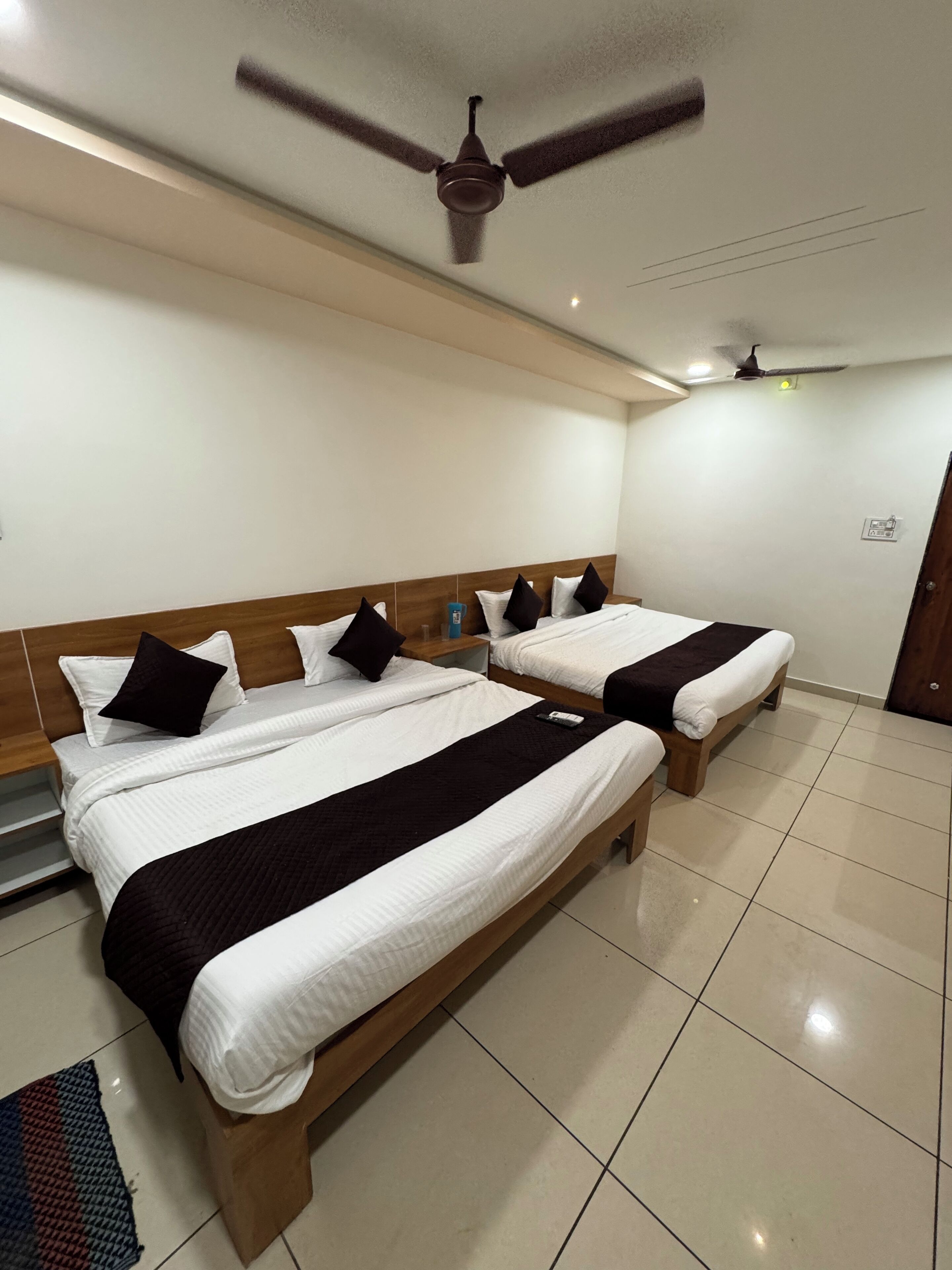 A hotel room with two beds, a ceiling fan, and a tiled floor.