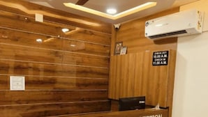 A reception area with a wooden reception desk, a ceiling fan, and an air conditioning unit. - Hotel Ayodhya Bhwan (Dwarka)