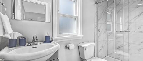 Ein Badezimmer mit einem weißen Waschbecken, einer Toilette und einer gläsernen Dusche.