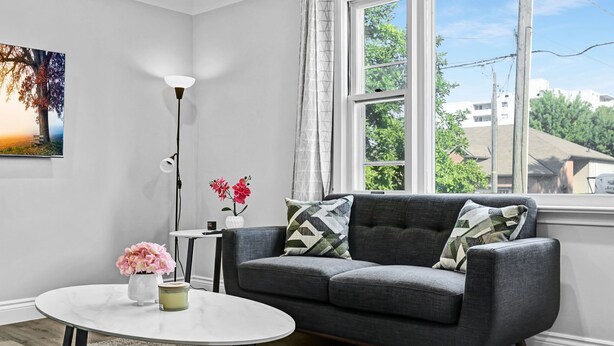 Ein modernes Wohnzimmer mit einem grauen Sofa, einem runden Couchtisch, einer Stehlampe und einem Gemälde an der Wand.