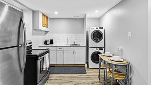 Eine kompakte Küche mit Edelstahl-Kühlschrank, einem Kombi-Backofen, einer Waschmaschine und einem kleinen Esstisch mit Stühlen.
