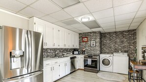 A modern kitchen with stainless steel appliances, white cabinets, a stone backsplash, and a wooden dining table. - Rustic Cowboy Ranch Retreat: Stay Near Nashville (Antioch)