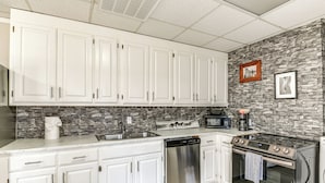 A kitchen with white cabinets, a dishwasher, a microwave, a stove, and a stone backsplash. - Rustic Cowboy Ranch Retreat: Stay Near Nashville (Antioch)