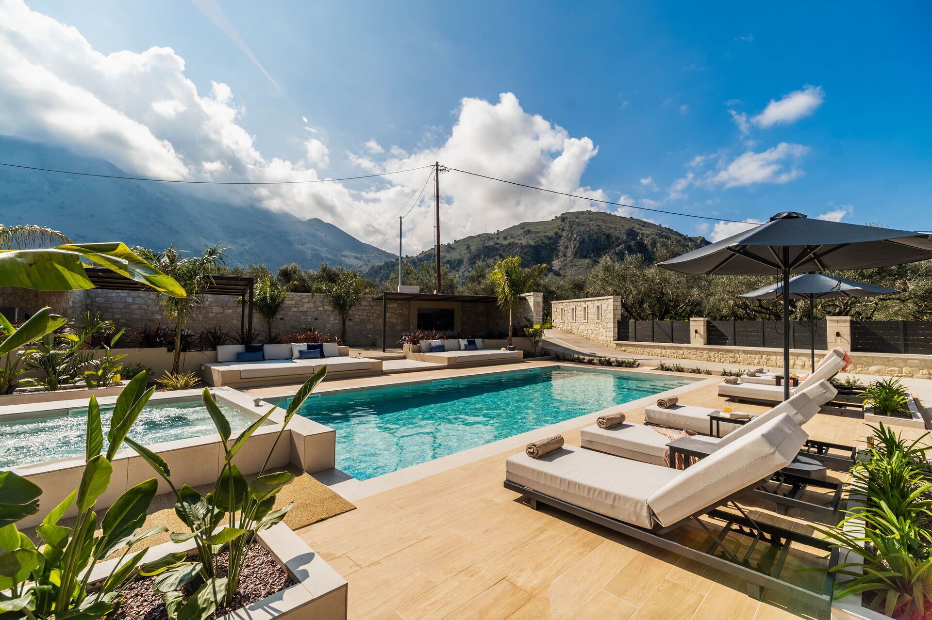 A pool area with lounge chairs, a stone wall, and a mountain backdrop.