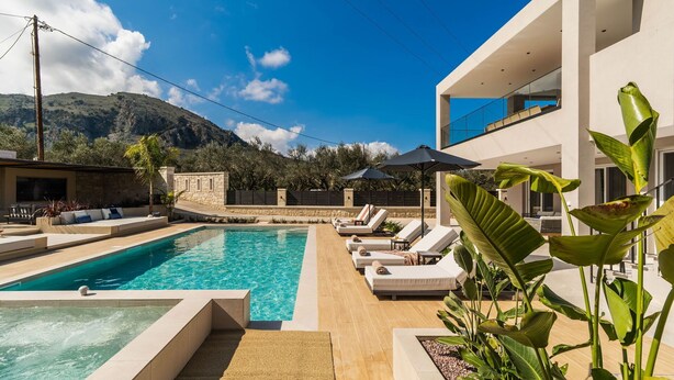 A modern pool area with lounge chairs and umbrellas, surrounded by a stone wall and lush greenery. - Villa Serenity- Modern villa for an exclusive vacation in Crete (Kournás)