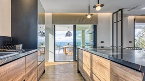 A modern kitchen with a large island, wooden cabinetry, and a view of the ocean.