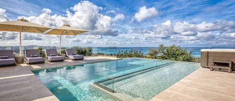 Piscina cristalina com espreguiçadeiras e guarda-sóis, com vista para um oceano deslumbrante.