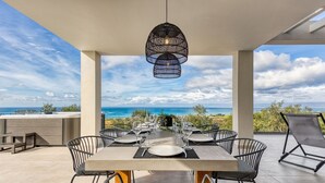 An outdoor dining area with a table set for six, surrounded by chairs, overlooking a scenic ocean view.