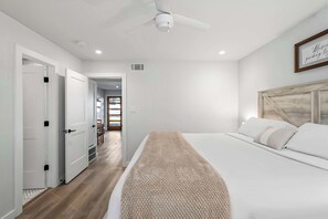 Un dormitorio con cama, ventilador de techo y puerta que da a otra habitación.