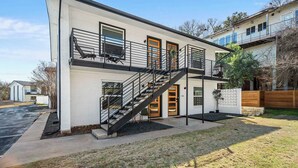 Una casa moderna de dos pisos con un balcón, una escalera y un pequeño jardín delantero.