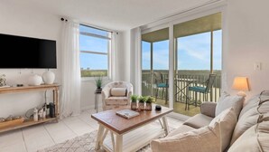 A spacious living room with a flat-screen TV, a wooden coffee table, a sofa, and a balcony with outdoor seating.