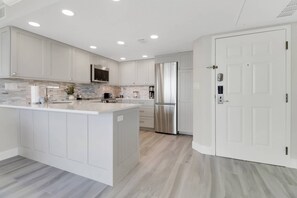 Una cocina moderna con armarios blancos, una isla central, un refrigerador de acero inoxidable y un microondas.