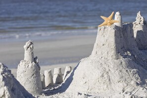 Ein Sandburg mit einem Seestern darauf, auf einem Strand mit dem Ozean im Hintergrund.