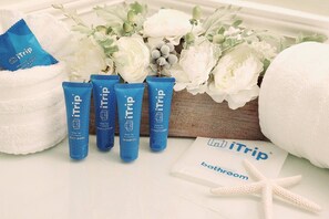 Artículos de aseo que incluyen loción corporal, acondicionador y champú, sobre una superficie blanca junto a un ramo de flores blancas y un adorno con forma de estrella de mar.