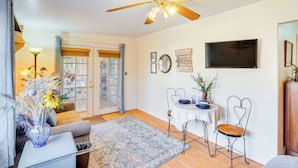A well-lit room with a ceiling fan, a dining table with chairs, a TV mounted on the wall, and a window with curtains. - Walkable Studio w/ Patio in Tucson! (Tucson)