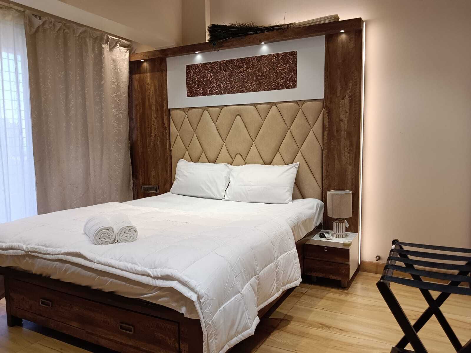 A neatly made bed with white linens, a headboard with a diamond pattern, and a bedside table with a lamp.