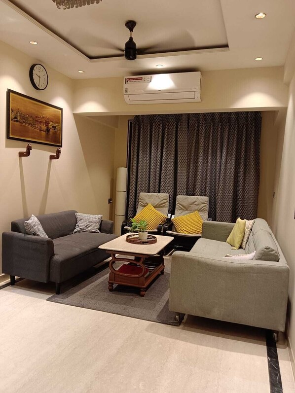 A living room with two sofas, a coffee table, a clock, and an air conditioning unit.