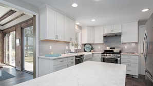 Une cuisine moderne avec des meubles blancs, un grand îlot en marbre et des appareils électroménagers en acier inoxydable.