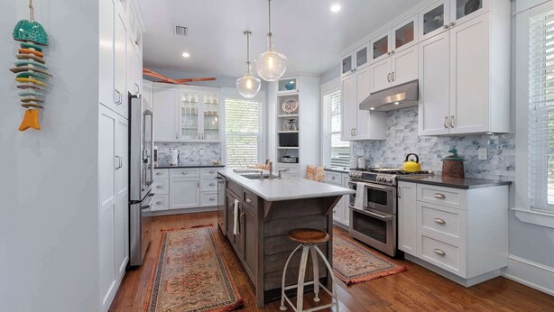 Une cuisine moderne avec des meubles blancs, un îlot central, une cuisinière et un luminaire suspendu.