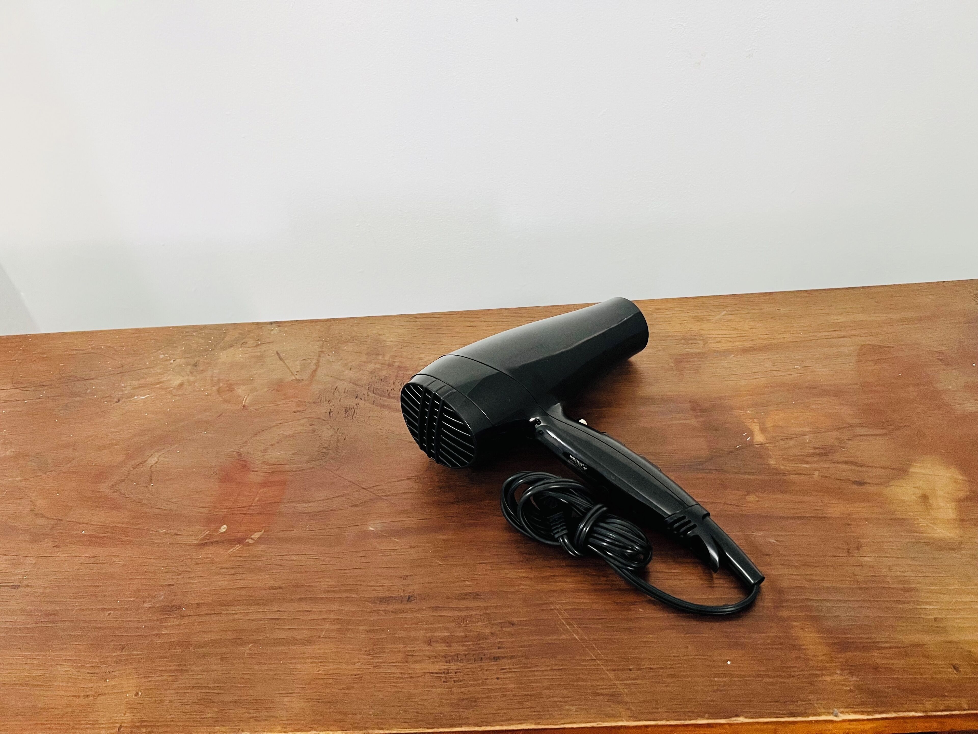 A black hair dryer with a cord on a wooden table.