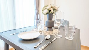 Et spisebord dækket med en hvid tallerken, bestik og klare glas, med en vase med blomster i midten.