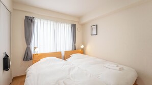 Et soveværelse med en dobbeltseng, et sengebord med lampe, et vindue med gardiner og en lyskontakt på væggen.