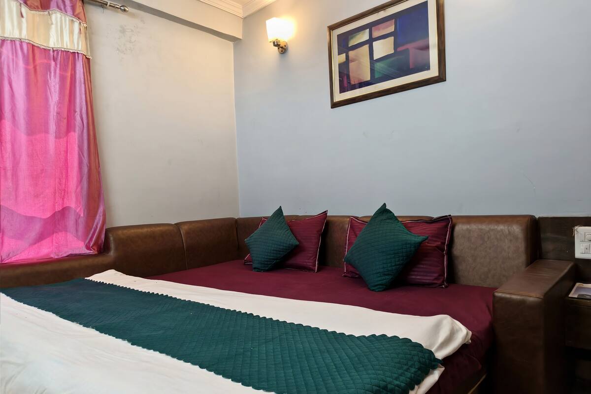 A bedroom with a bed, pillows, a blanket, a wall-mounted light, and a framed picture.