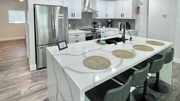 Une cuisine moderne avec des meubles blancs, des appareils en acier inoxydable et un îlot central doté de tabourets de bar.