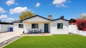 A modern house with a well-maintained lawn, a patio with chairs, and a clear blue sky. - Modern Central PHX Home / 4 Bed 2 Bath / Sleeps 10 (Phoenix)