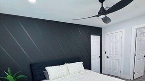 Une chambre à coucher avec un lit, un ventilateur de plafond, une plante en pot et une porte.