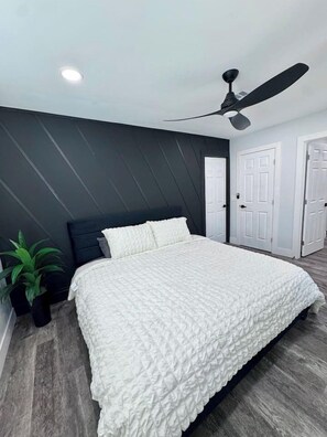 Une chambre à coucher avec un lit, un ventilateur de plafond, une plante en pot et une porte.