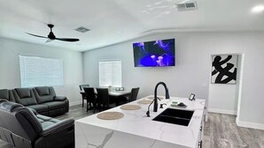 A modern living room with a kitchen island, a black leather sofa, a dining area, and a flat-screen TV. - Modern Central PHX Home / 4 Bed 2 Bath / Sleeps 10 (Phoenix)
