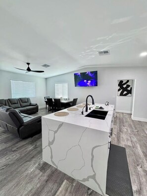 A modern living room with a kitchen island, a black leather sofa, a dining area, and a flat-screen TV. - Modern Central PHX Home / 4 Bed 2 Bath / Sleeps 10 (Phoenix)