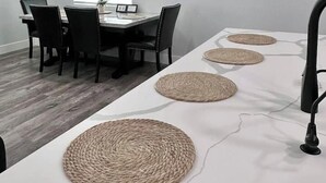 A dining area with a long table, black chairs, woven placemats, and a wall-mounted TV displaying jellyfish. - Modern Central PHX Home / 4 Bed 2 Bath / Sleeps 10 (Phoenix)