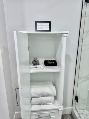 A white wardrobe with a sign above it, a glass shower enclosure, and a marble-tiled shower area.