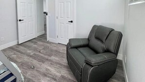 Une pièce avec un ventilateur de plafond, des murs blancs, un plancher gris et un fauteuil en cuir noir.