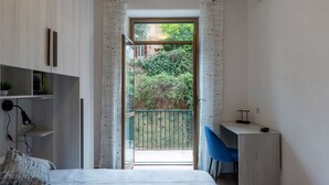 A bedroom with a bed, a desk, and a view of a balcony with greenery. - GuestHost - Garbatella Apartment - Roma (Roma)